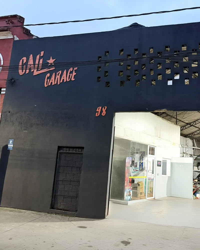 Fachada da Cali Garage em Santos, com o letreiro e o número 98 na parede preta e o portão aberto