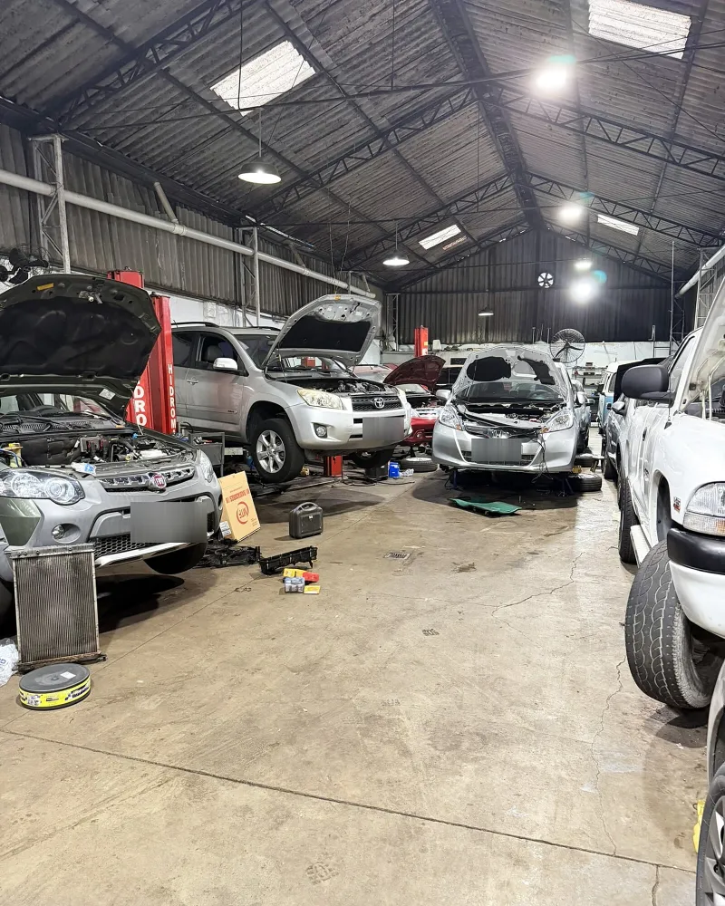Carros nos elevadores da oficina, com capôs abertos sob o telhado do galpão