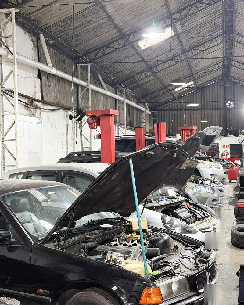Vários carros com o capô aberto em serviço no pátio coberto da oficina