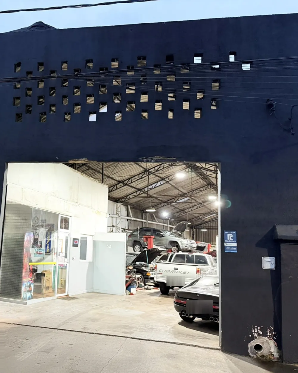 Entrada da Cali Garage ao entardecer, com a oficina iluminada ao fundo